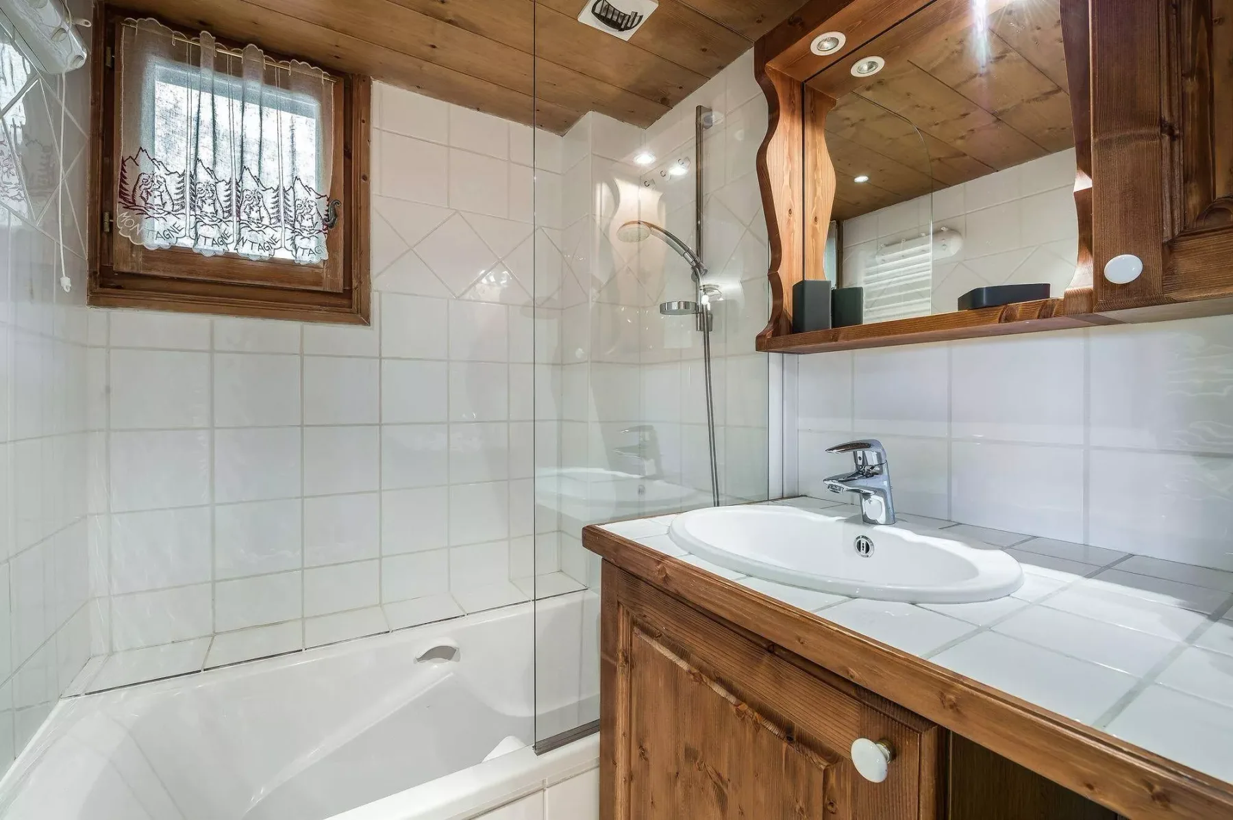 A tiled bathroom with a bathtub, sink, and wooden vanity.