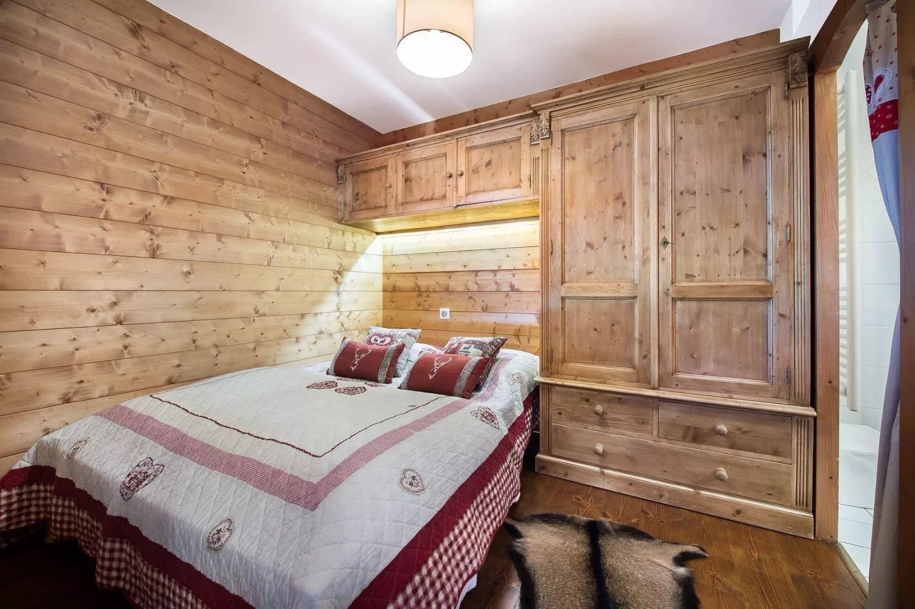 A bedroom with a double bed beside a large wooden wardrobe.