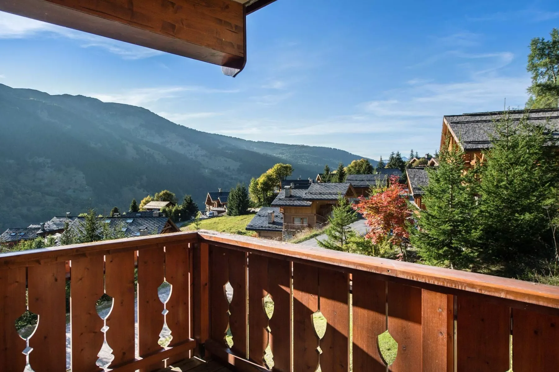 A wooden balcony overlooks mountain scenery and nearby buildings.