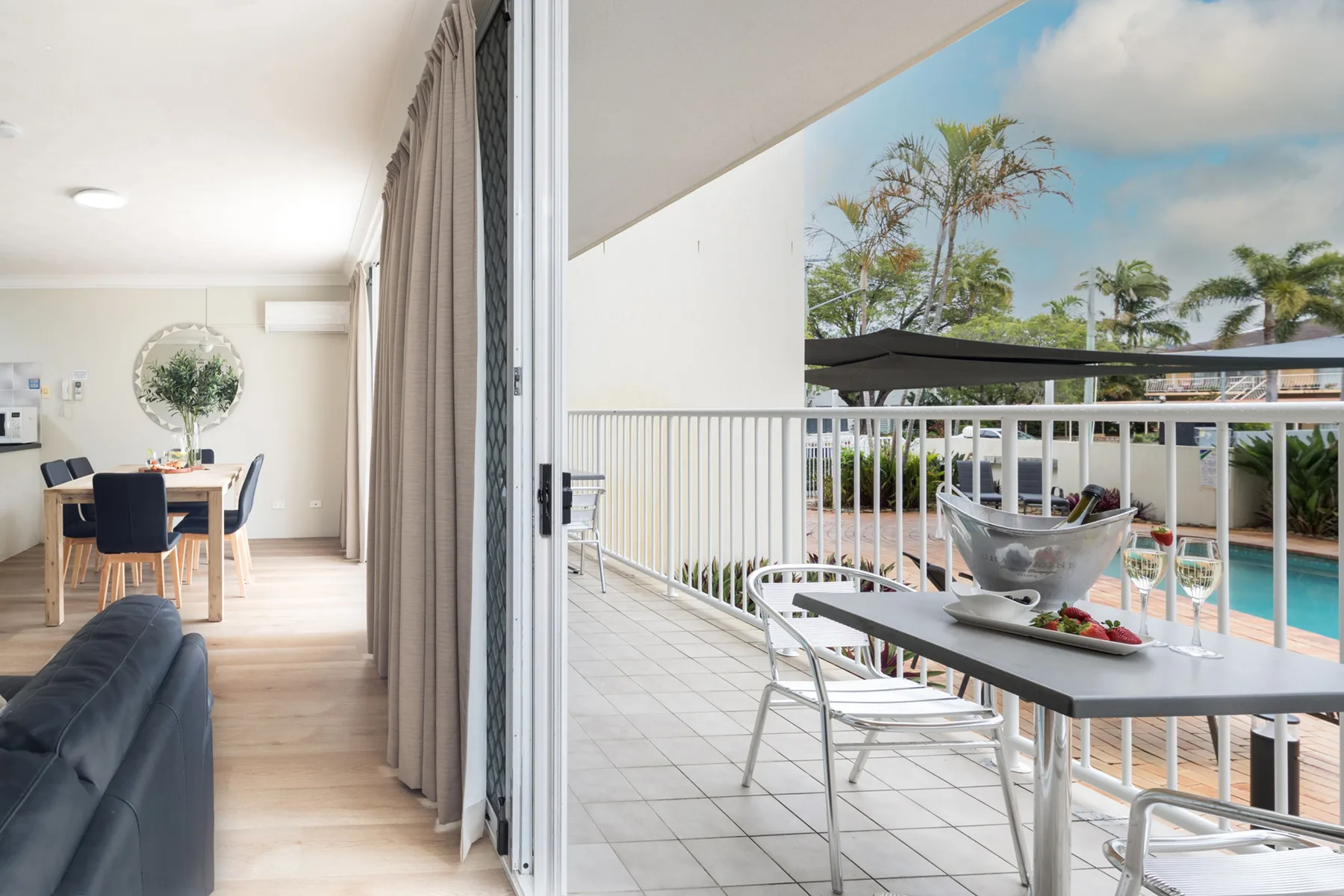 Un comedor se abre a un balcón embaldosado con vistas a una piscina.