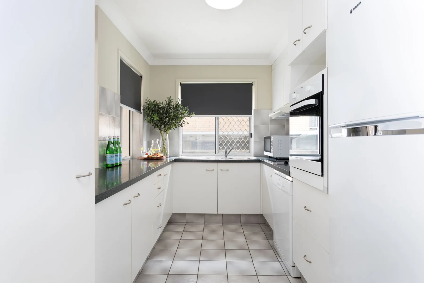 Una cocina luminosa con gabinetes blancos, encimeras oscuras y una ventana.