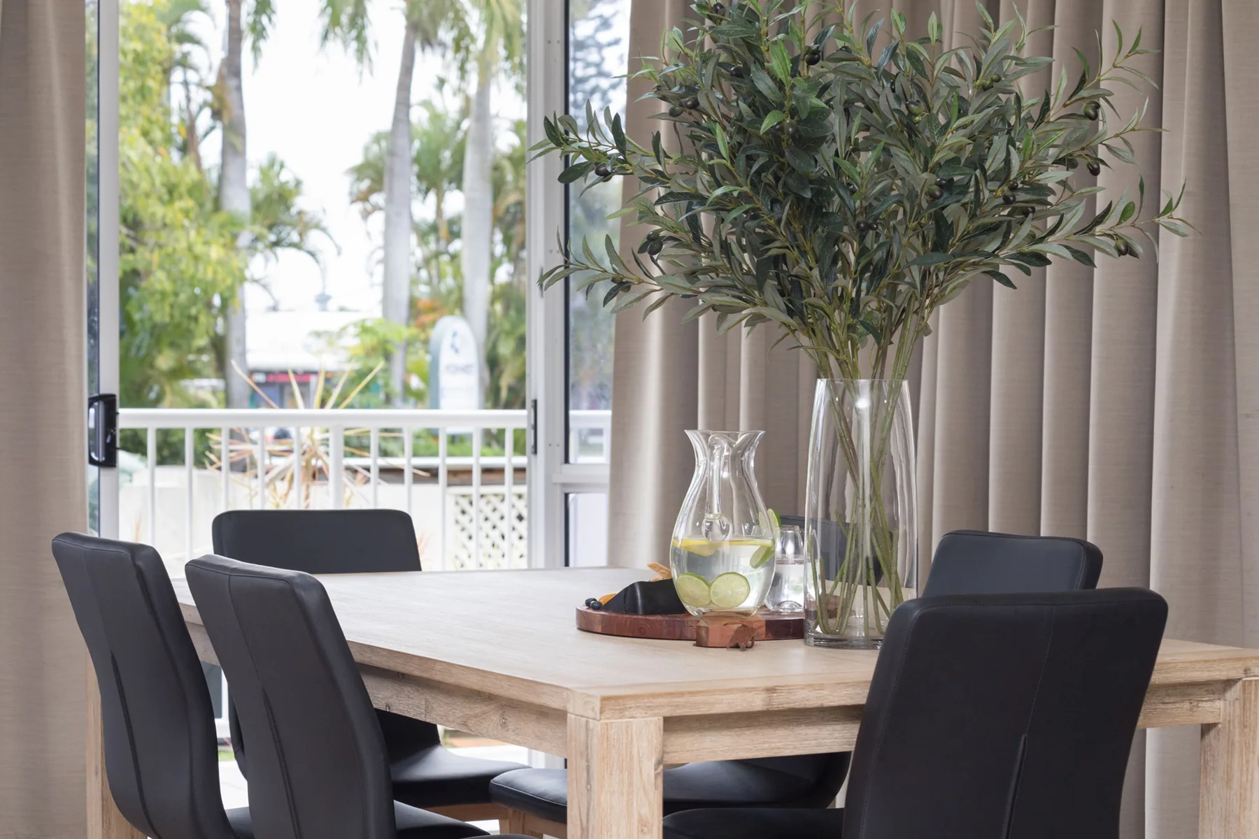 Comedor con una mesa de madera y asientos oscuros junto a grandes ventanales.