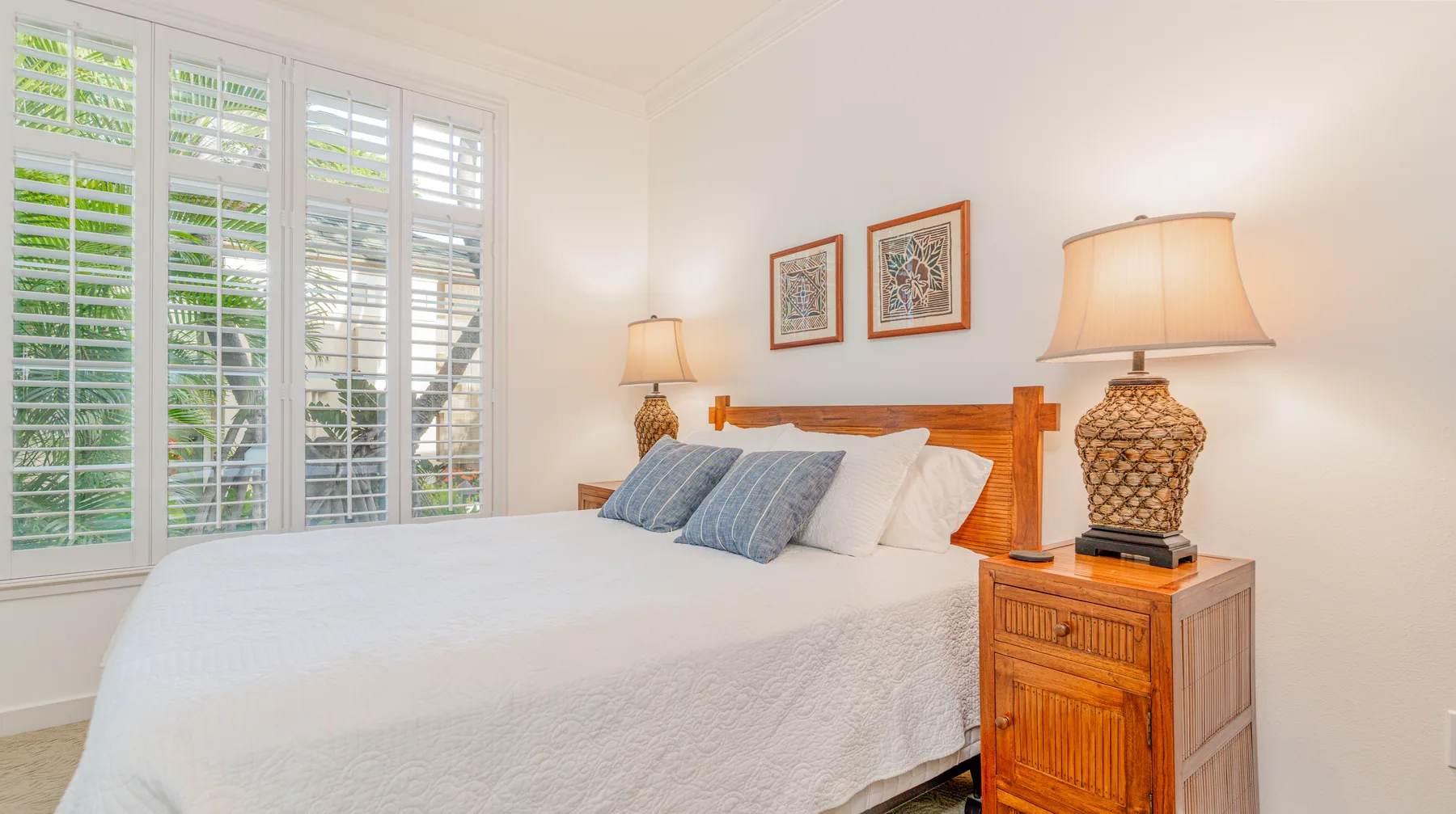 A bright bedroom with a bed, shuttered windows, and bedside lamps.