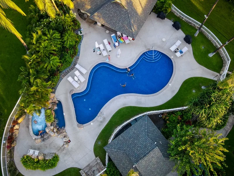 Vista aérea de una piscina rodeada por una terraza pavimentada y vegetación.