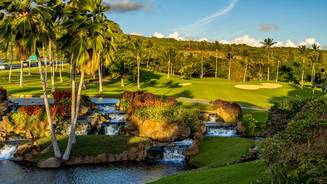 A landscaped golf course with a stream and small waterfalls in the foreground.