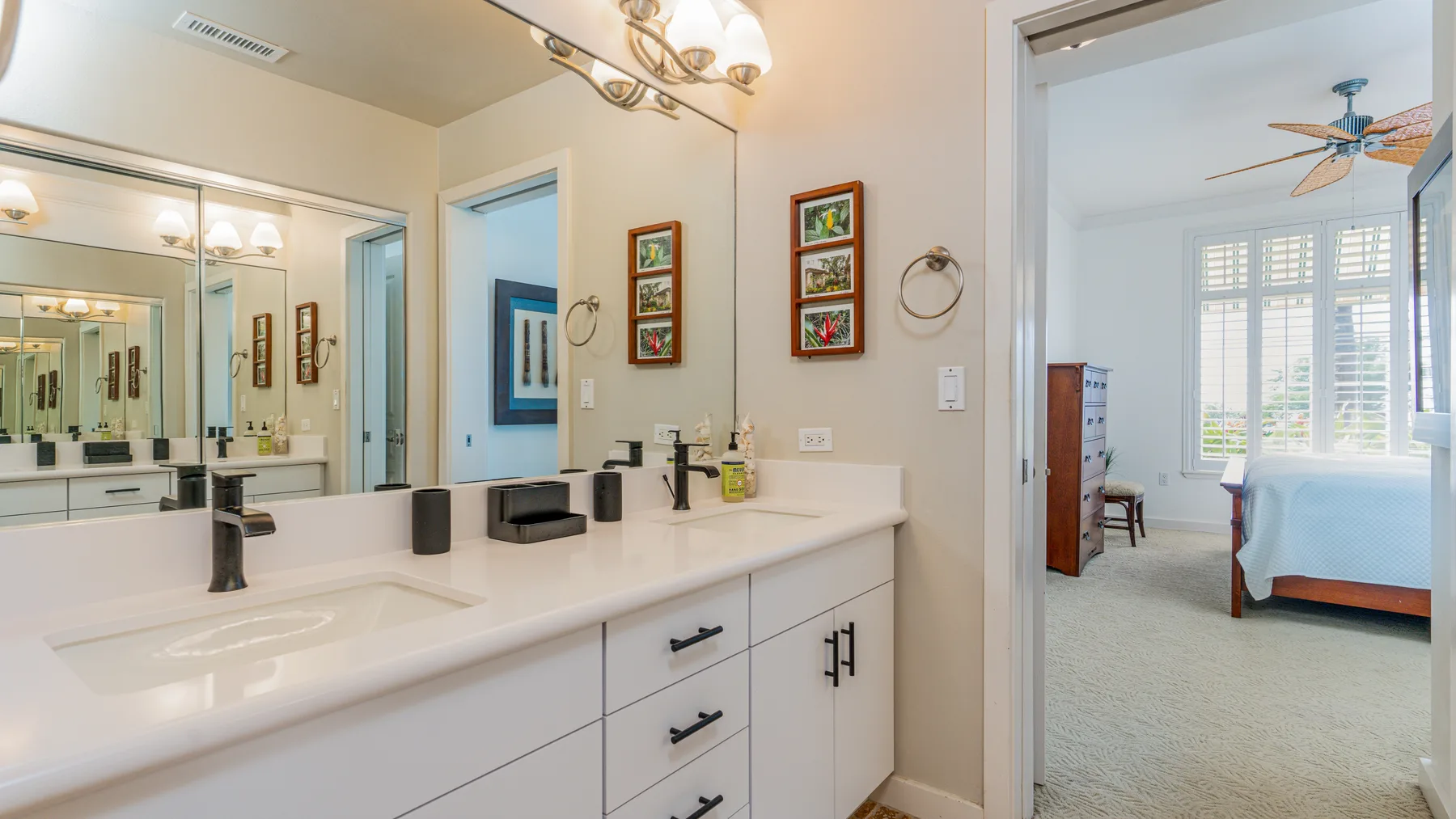 A bathroom vanity with a wide mirror opens onto a bedroom.