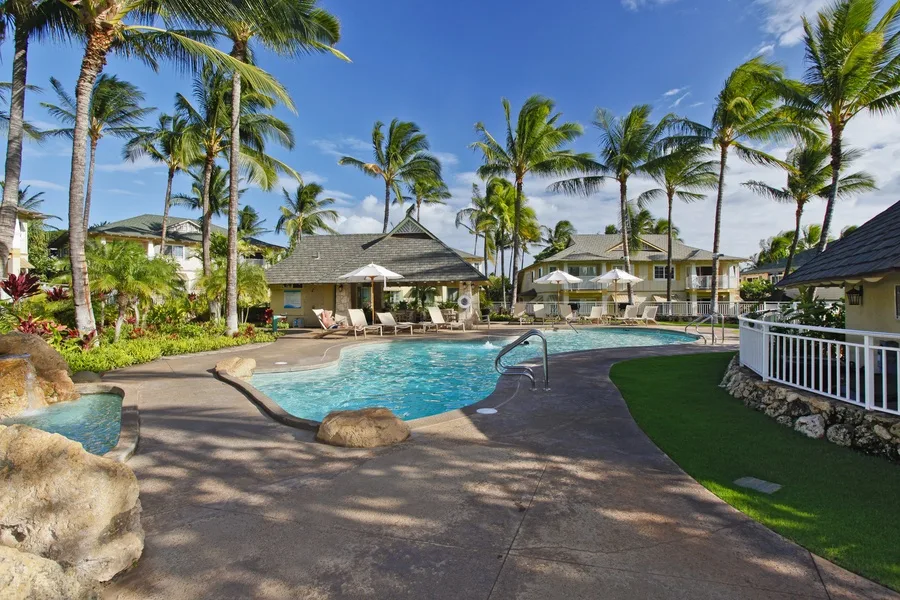A palm-lined outdoor swimming pool with lounge seating and surrounding tropical landscaping.