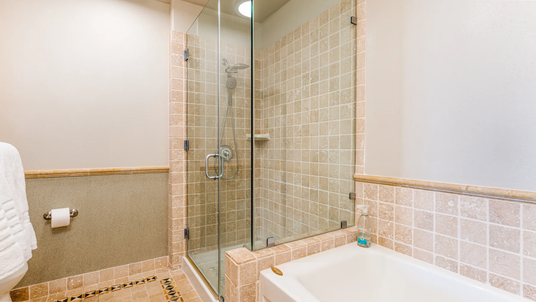 A tiled bathroom features a bathtub and glass-enclosed shower.