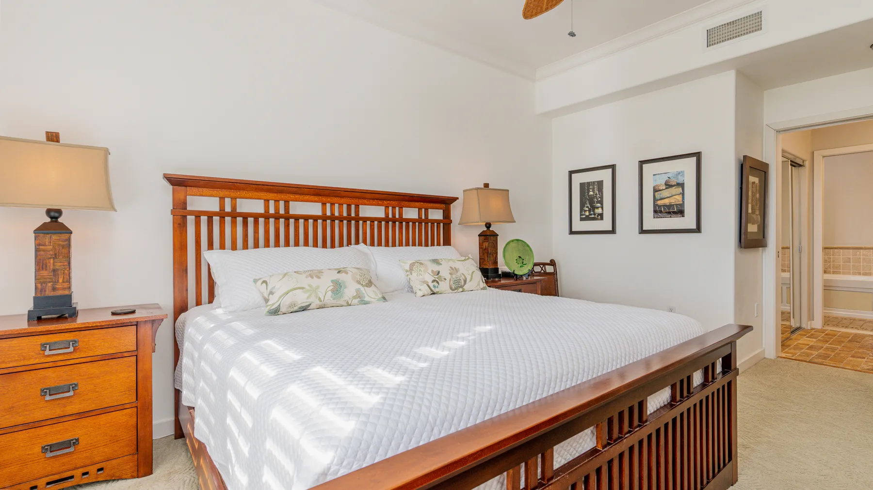 A bedroom with a large bed, wooden headboard, and framed pictures on the wall.