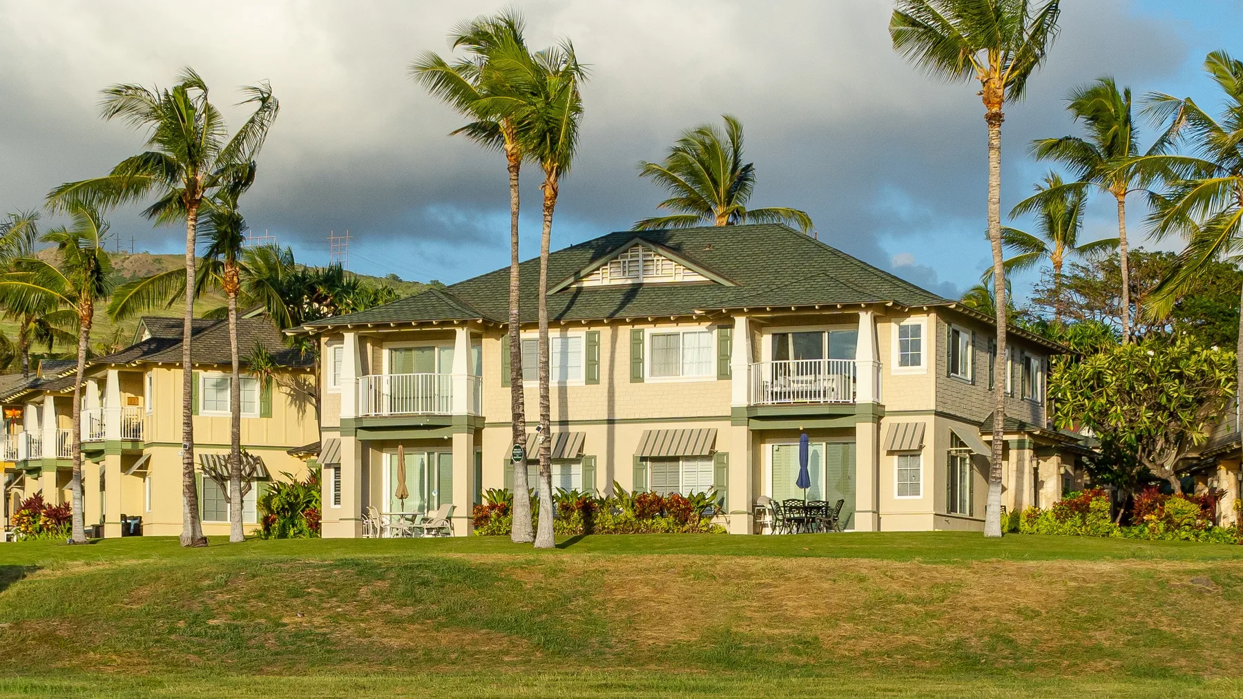 A two-story building with balconies stands behind a grassy lawn and palm trees.