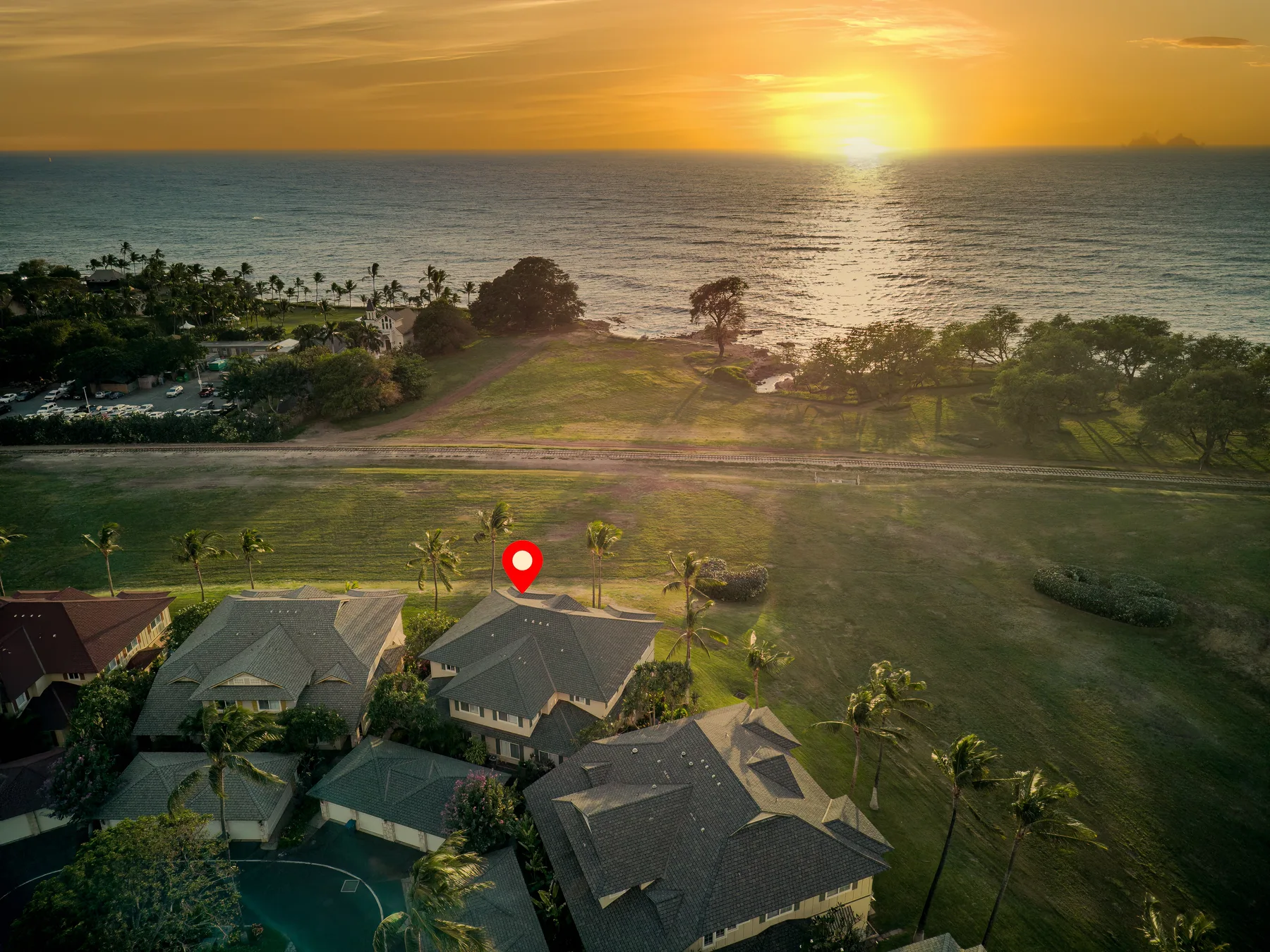 Aerial view of homes beside a broad green lawn, with the ocean at sunset.