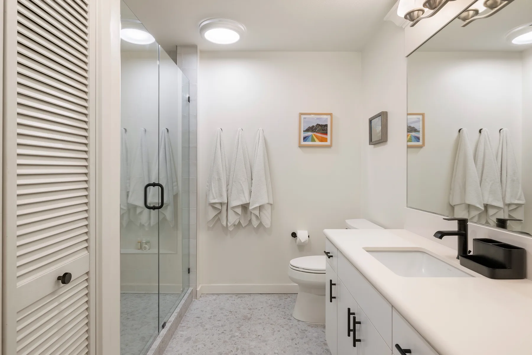 A bright bathroom with a glass shower, toilet, and long vanity.