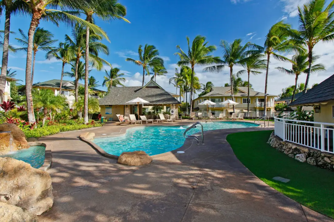 A curved swimming pool sits among palm trees and low resort buildings.