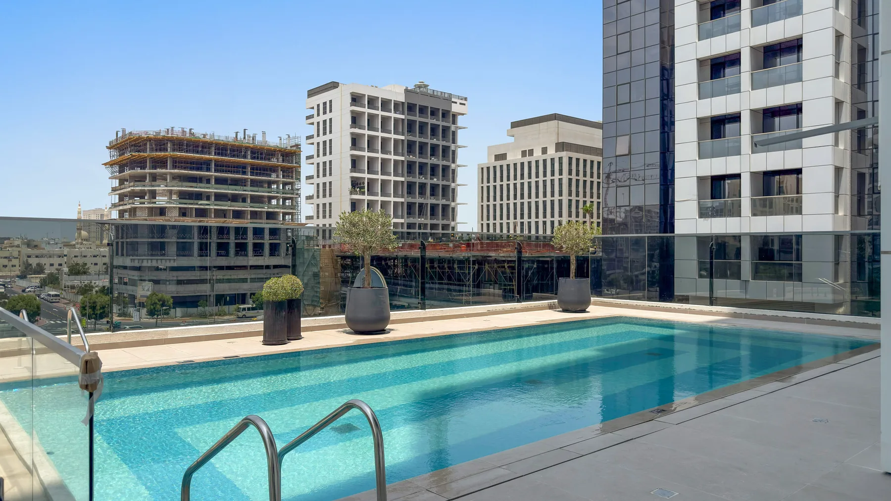 Una piscina en la azotea ofrece vistas de varios edificios modernos bajo un cielo despejado.