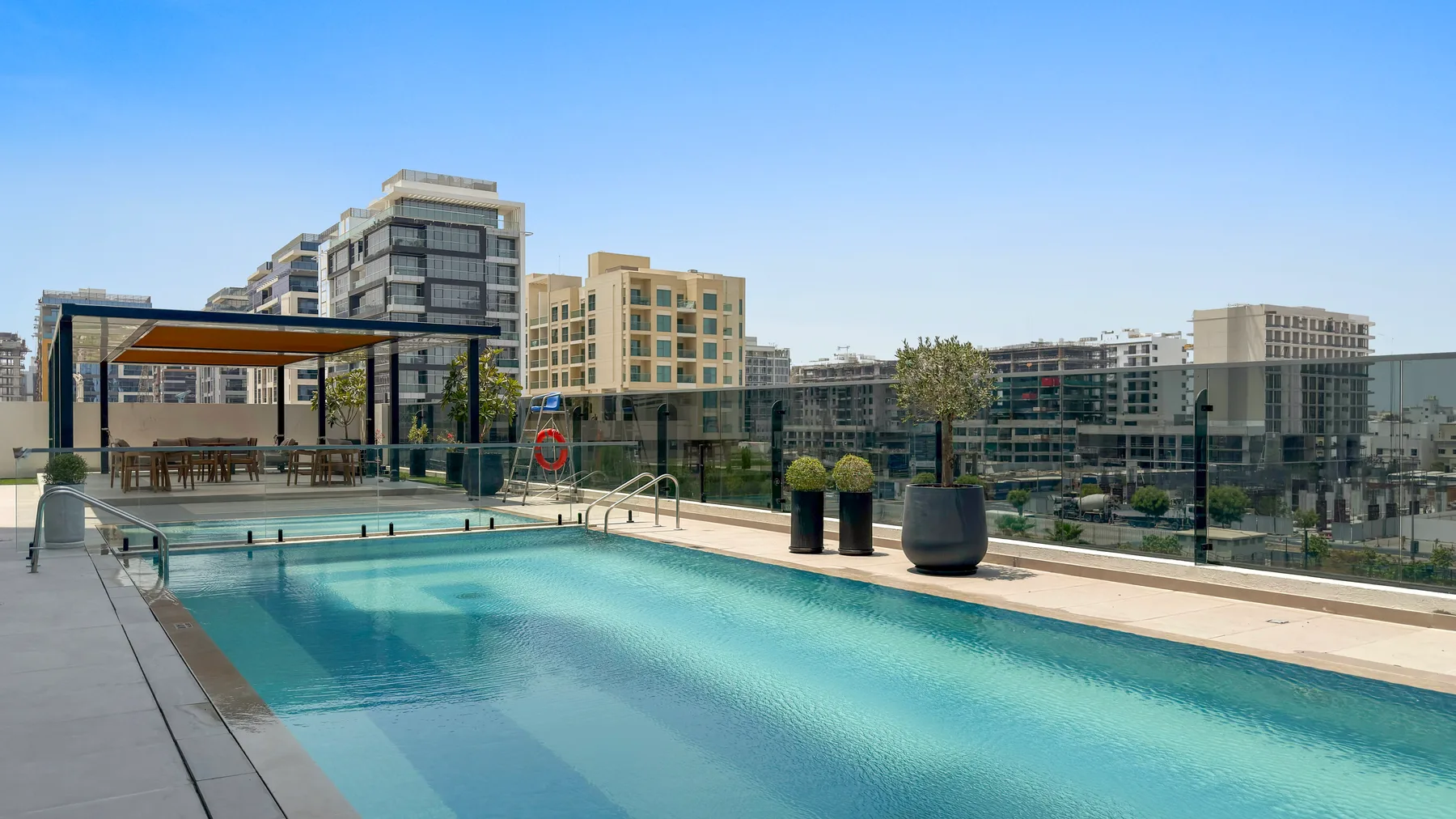 Una piscina en la azotea junto a una zona de asientos con sombra y edificios modernos.