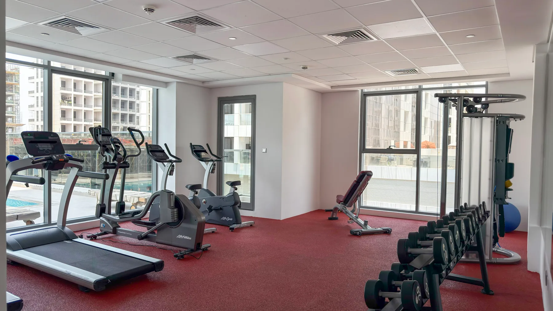 Un gimnasio con cintas de correr, máquinas de ejercicio y pesas sobre un suelo rojo.