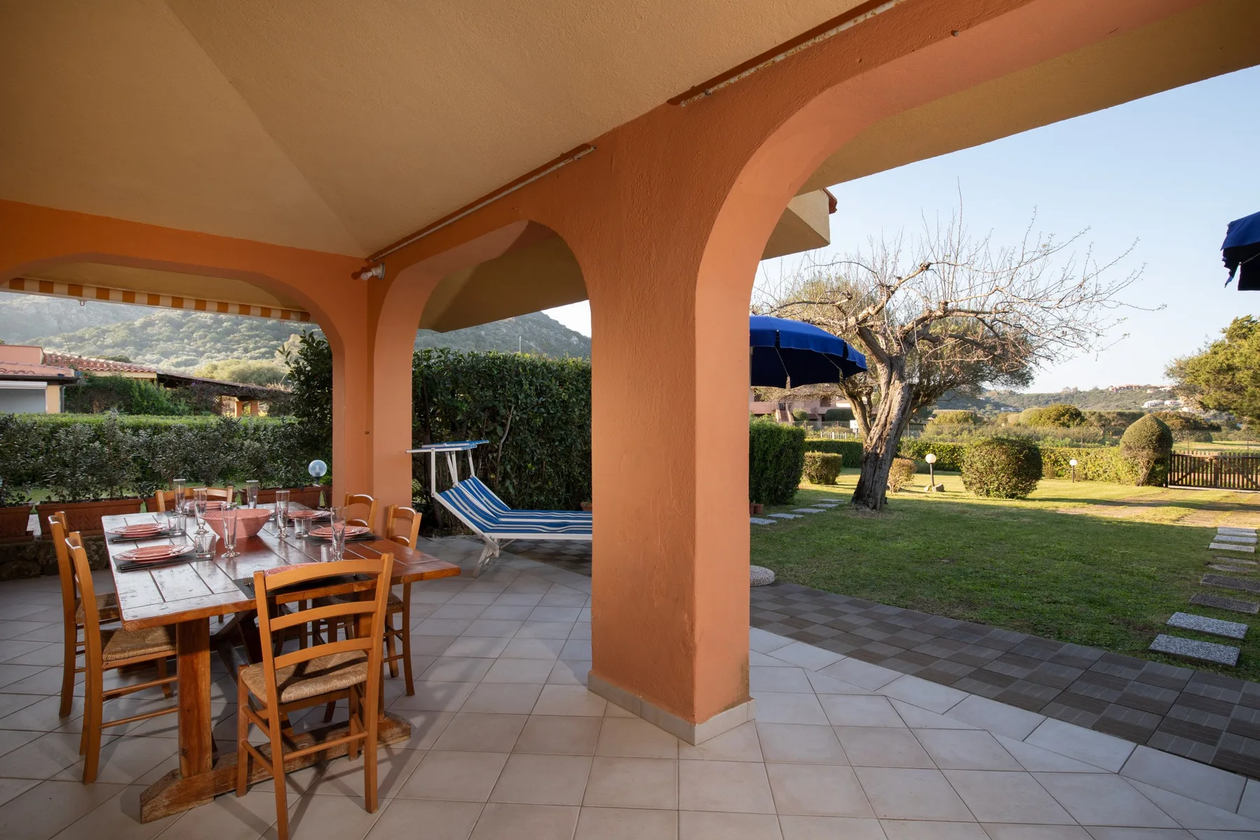 A covered patio with a dining table and chairs overlooks a garden.