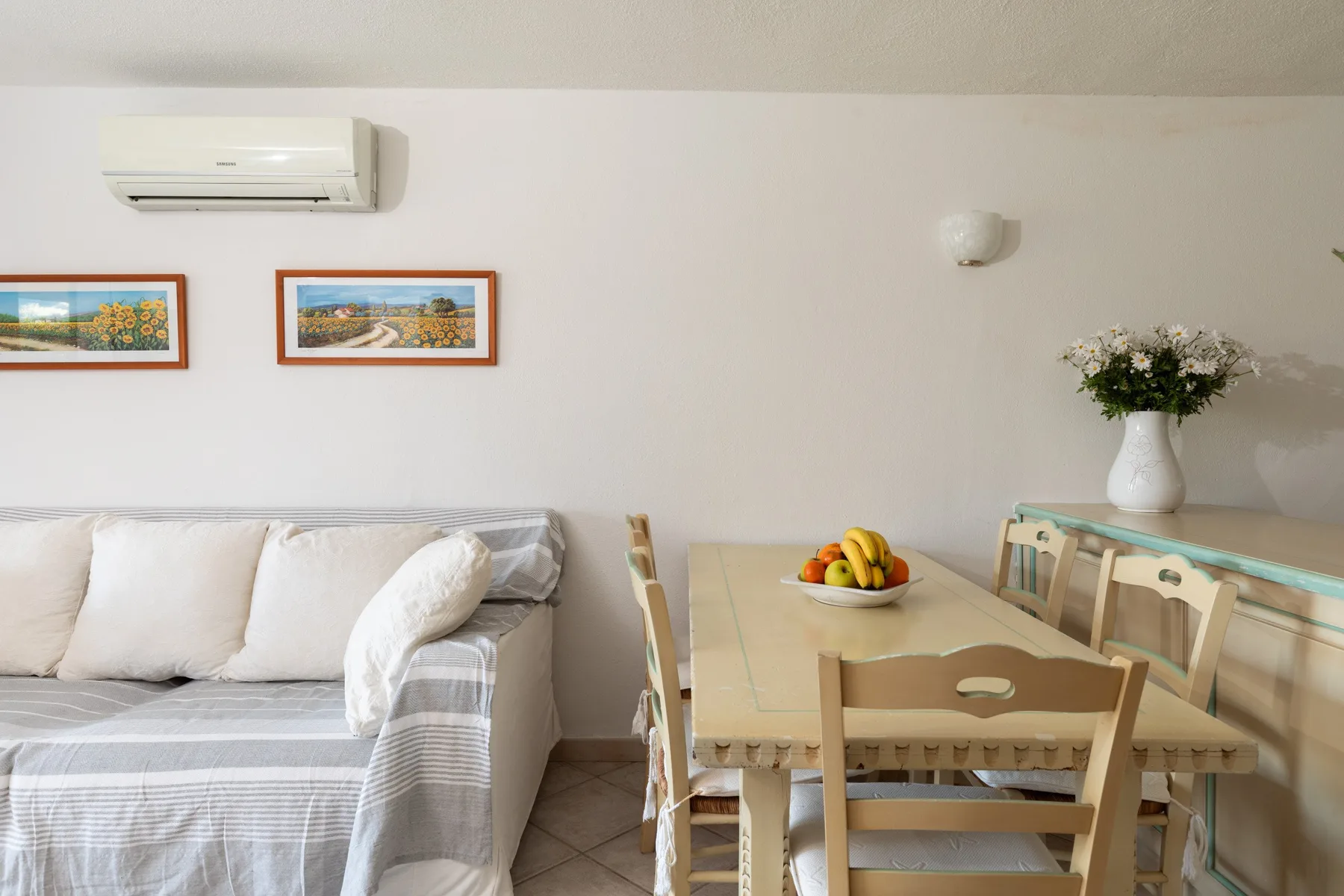 A dining table and seating sit beside a sofa in a bright room.