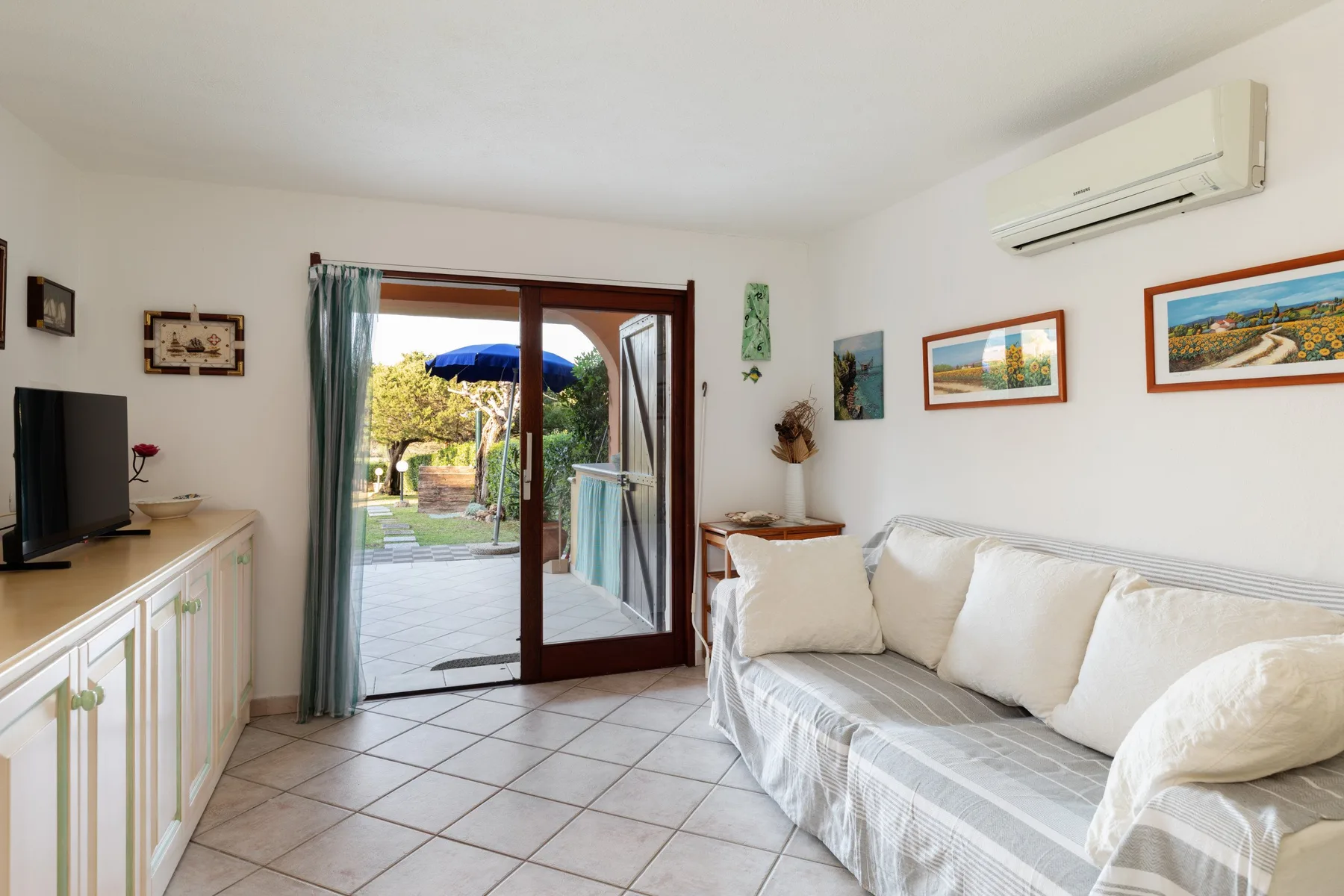 A bright living room with a cushioned sofa and glass doors opening to a patio.