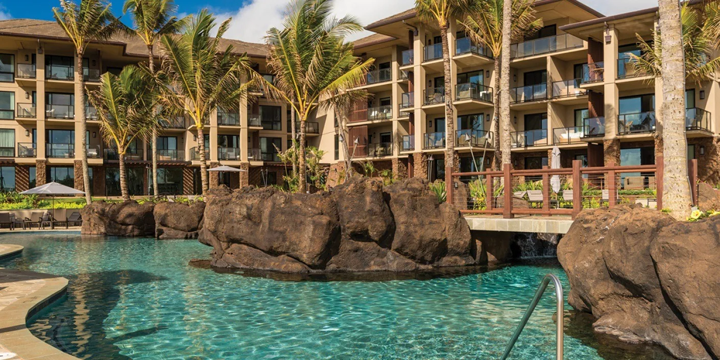 Una piscina con rocas decorativas está frente a un edificio de varios pisos.