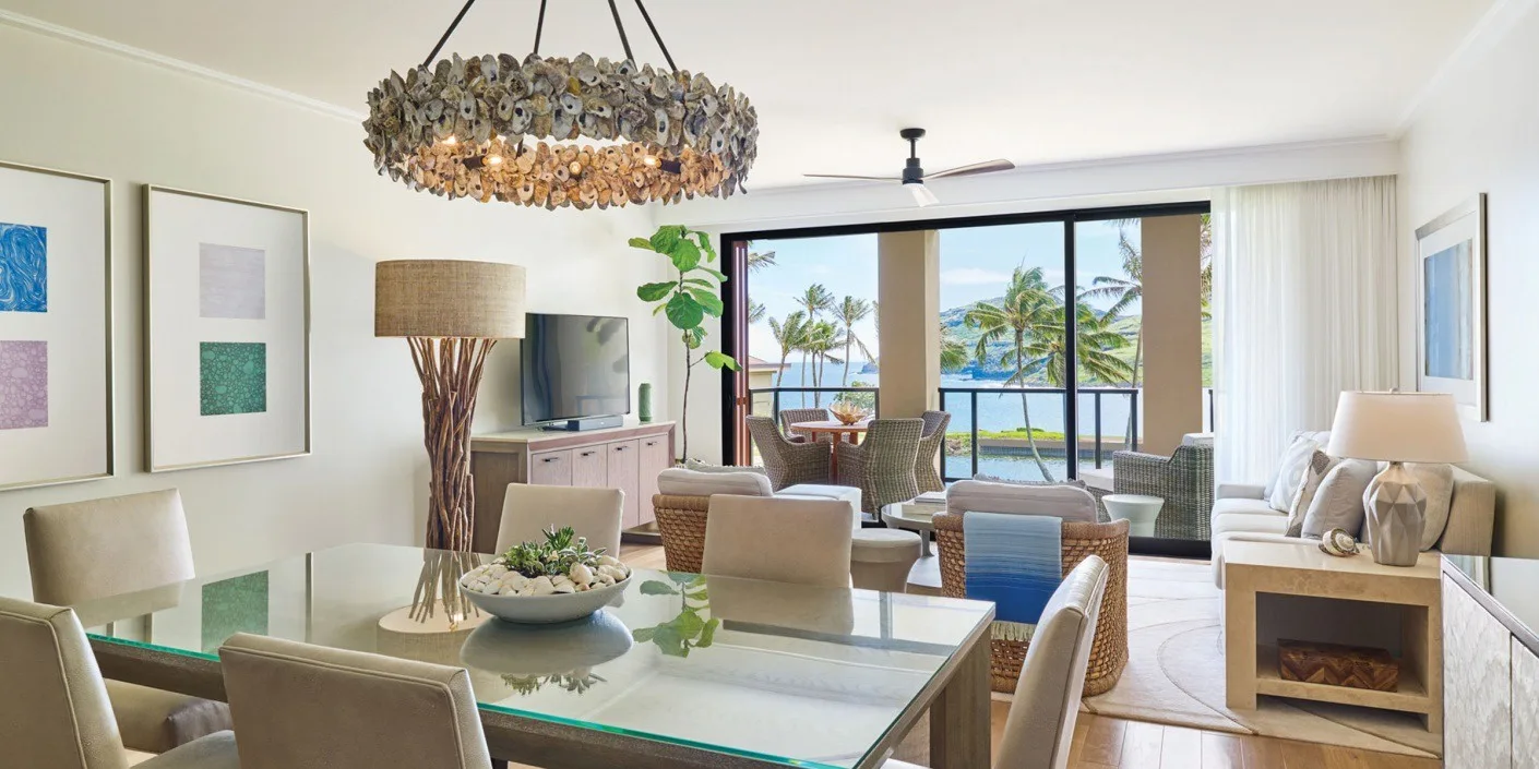 Una sala luminosa se abre a un balcón con palmeras y vistas al mar.