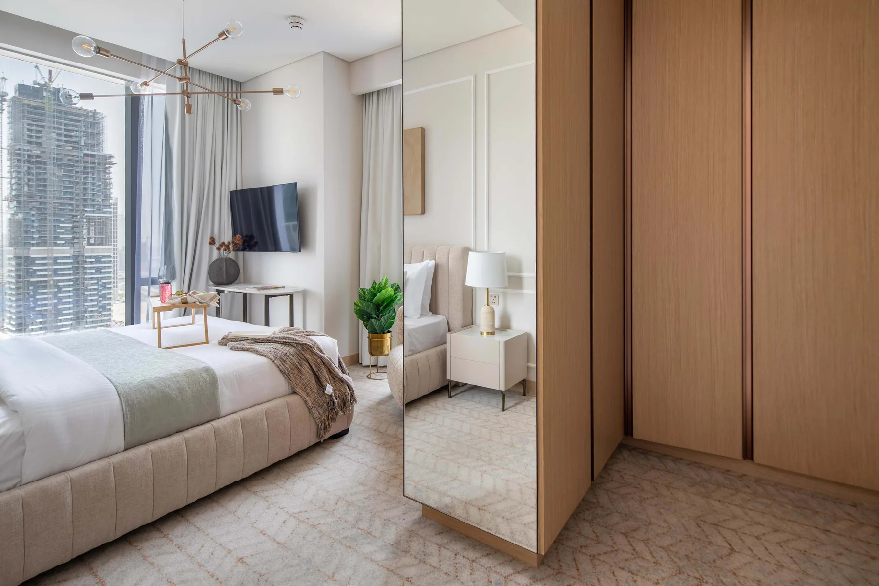 Un dormitorio luminoso con una cama, un televisor y grandes ventanas.