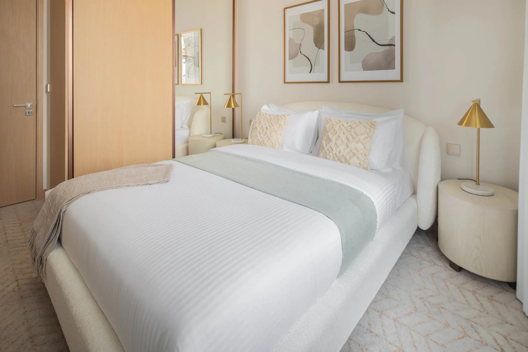 Un dormitorio luminoso con una cama bien hecha y cuadros abstractos enmarcados.