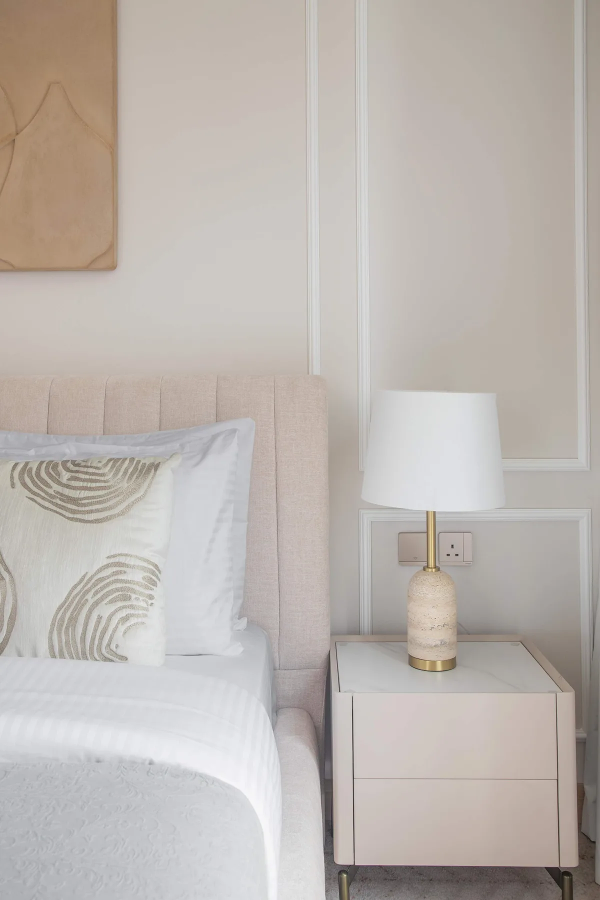 Un dormitorio con una cama, un cojín estampado y una mesita con una lámpara.