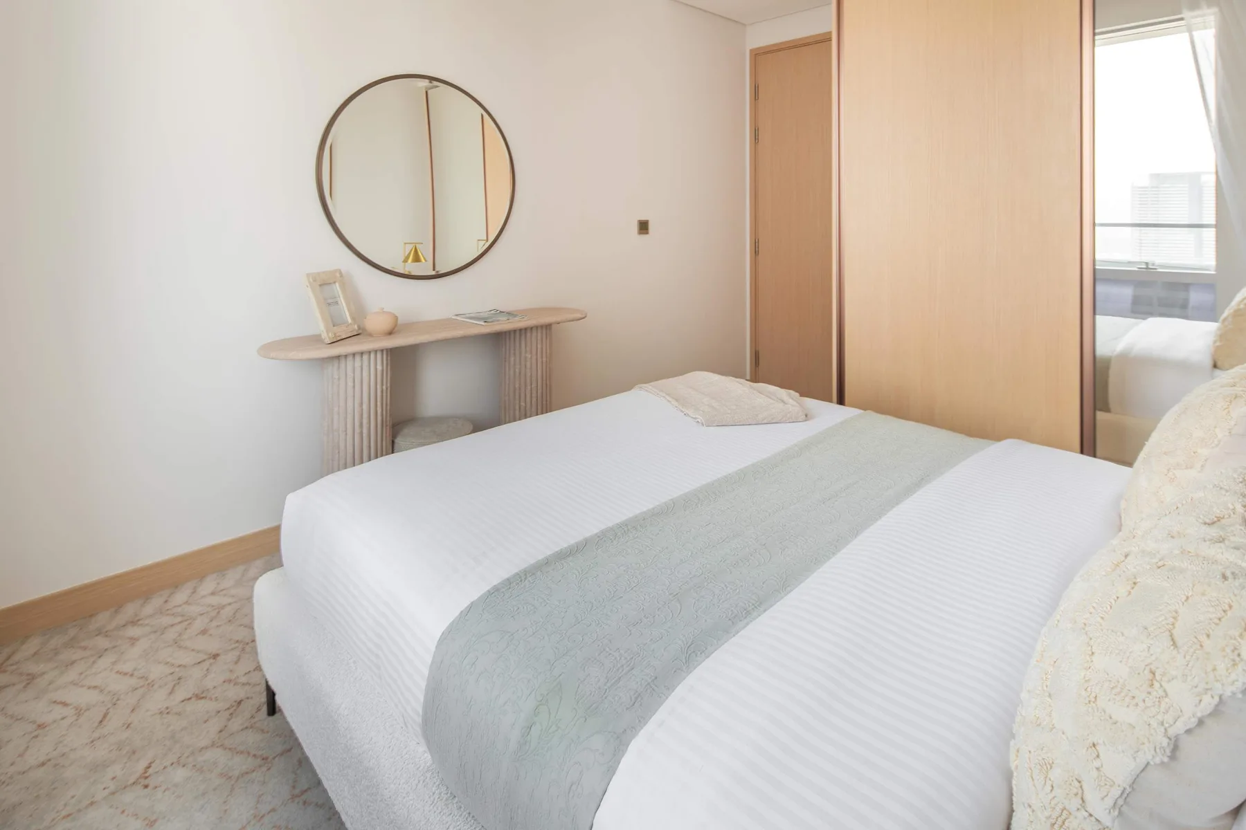Un dormitorio luminoso con una cama bien tendida y una pequeña mesa consola.