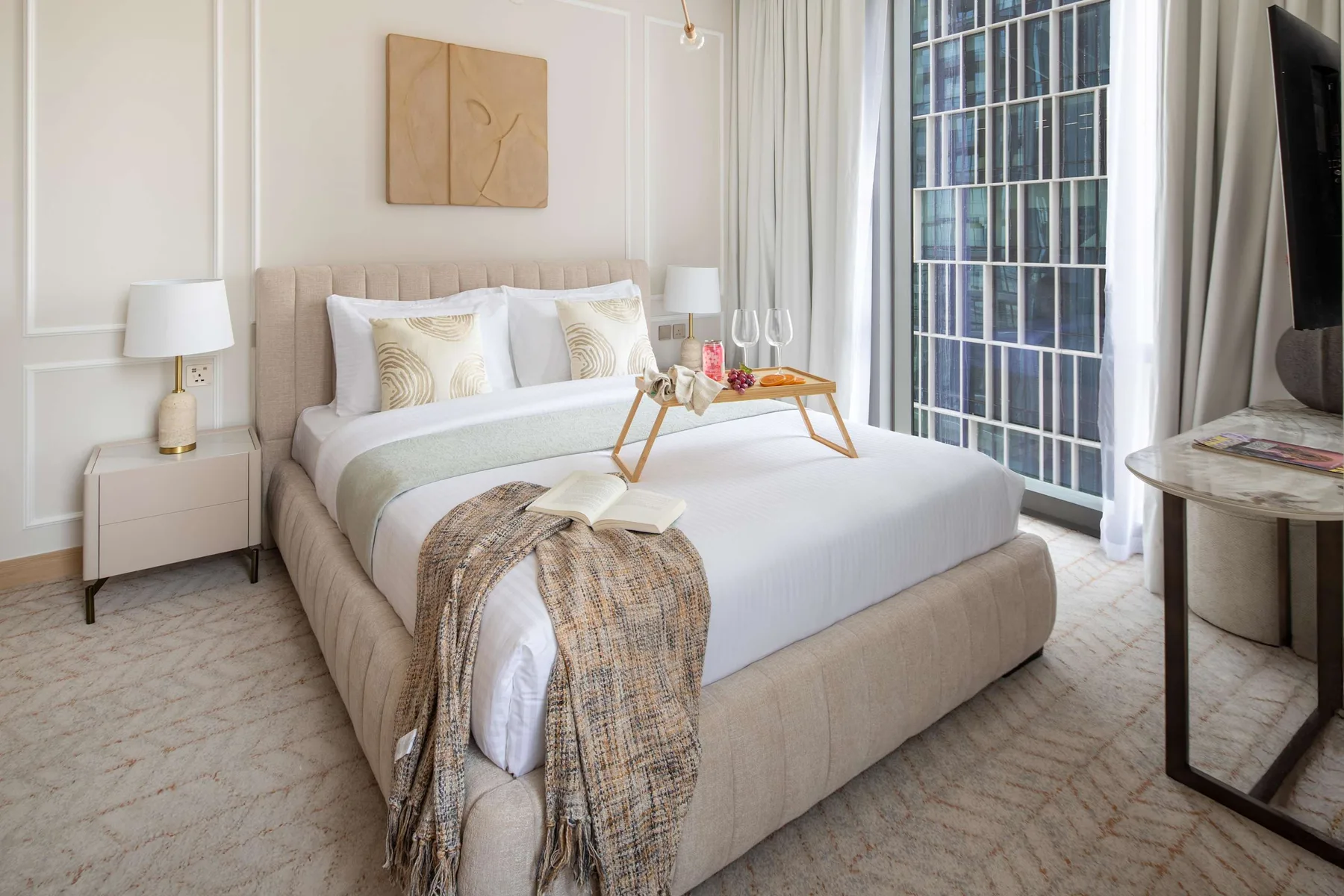 Un dormitorio con una cama bien tendida junto a una ventana grande.