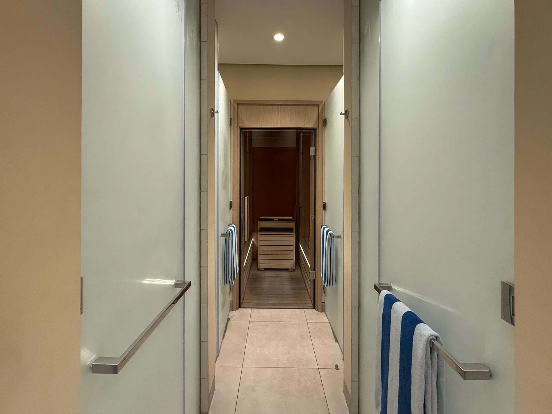 Un pasillo estrecho con suelo de baldosas y toallas colgadas en barras de pared.