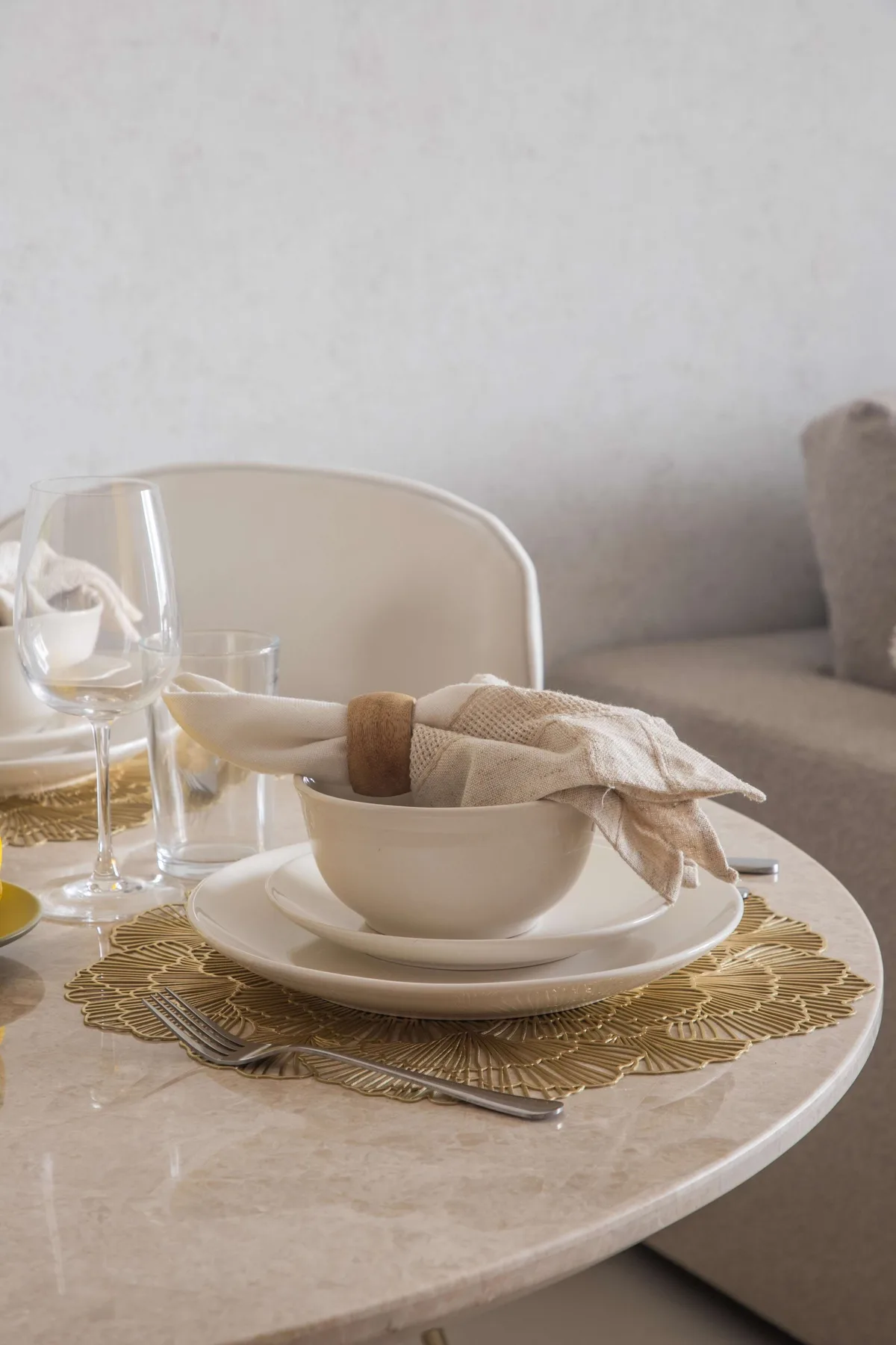 Una mesa de comedor está puesta con platos blancos, copas y una servilleta de tela doblada.
