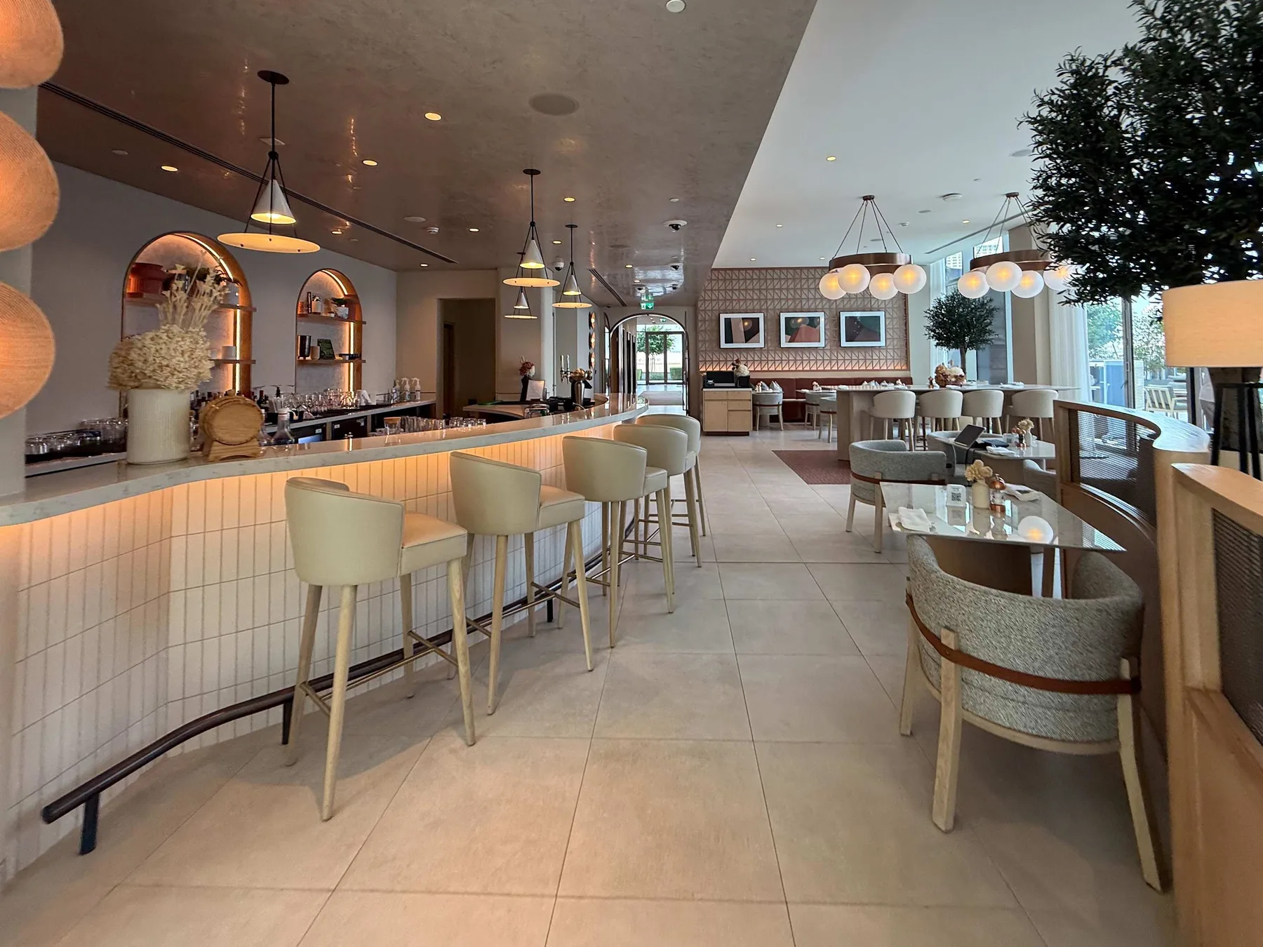 Un comedor de restaurante luminoso con una barra larga, mesas y grandes ventanales.
