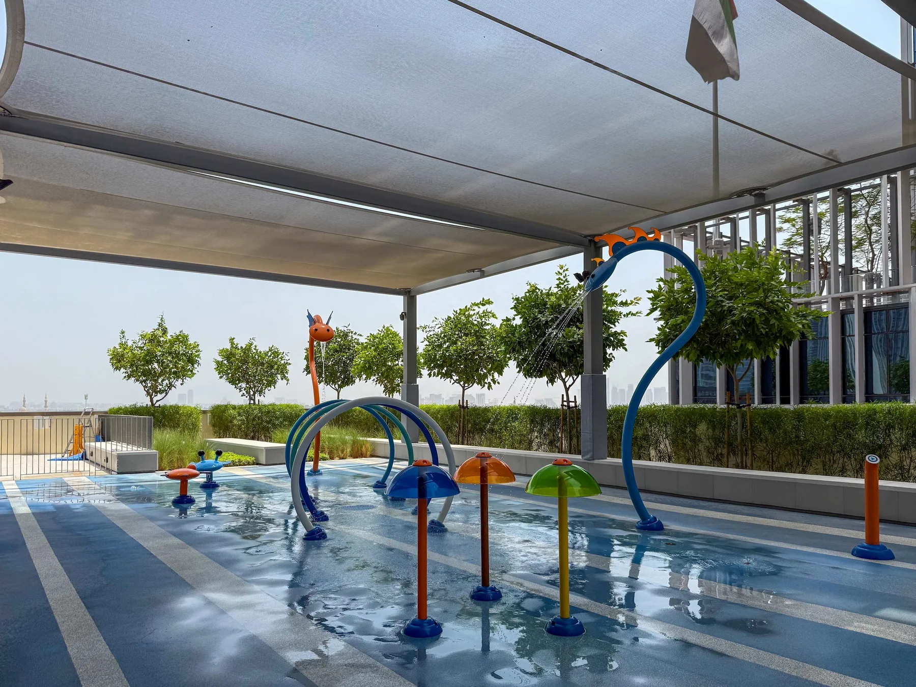 Una zona de juegos acuáticos al aire libre con elementos coloridos bajo una cubierta de sombra.