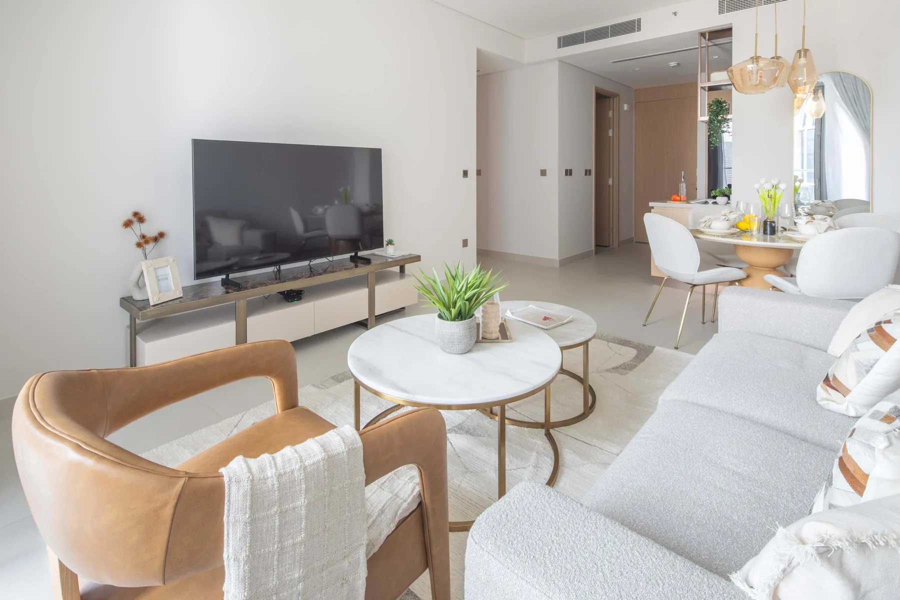 Una luminosa sala de estar y comedor con televisor, asientos y una mesa de centro redonda.