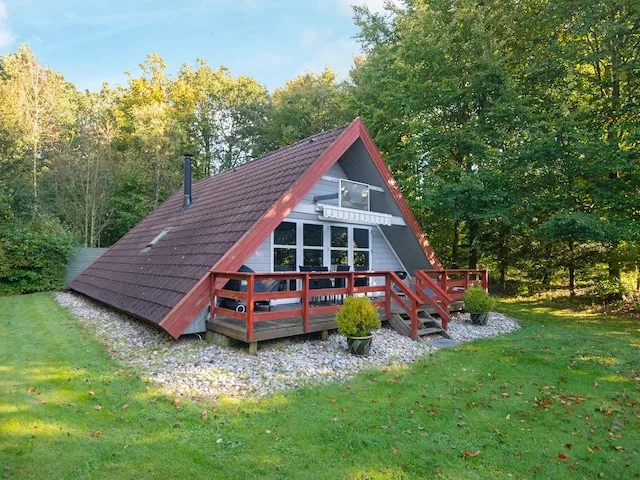 A red-trimmed cabin stands among trees beside a grassy lawn.