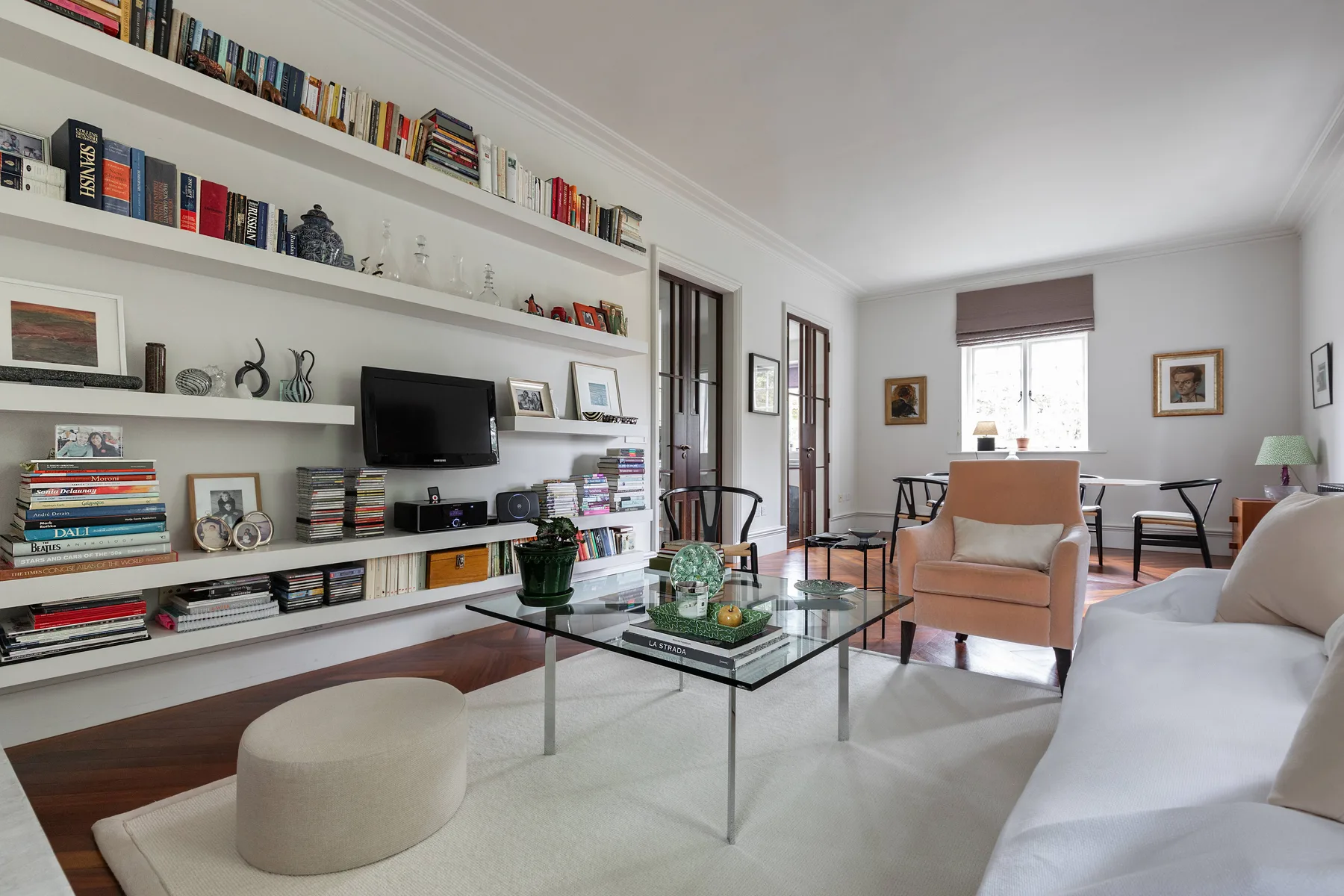 Una sala luminosa con estanterías de pared y una mesa de centro de vidrio.