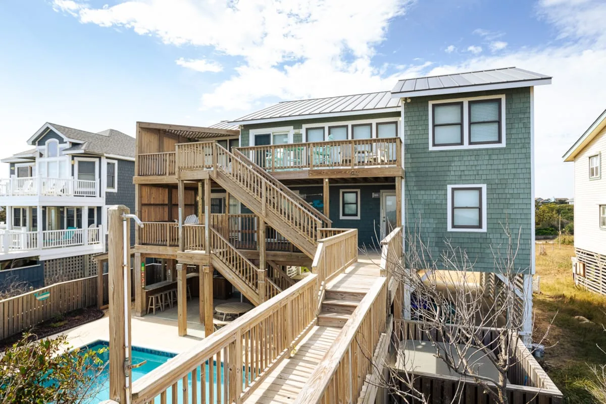 Una casa elevada con escaleras y terrazas de madera junto a una piscina pequeña.