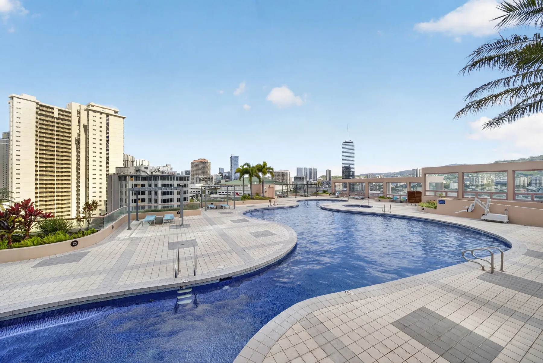 A rooftop swimming pool is surrounded by a tiled deck and city buildings.