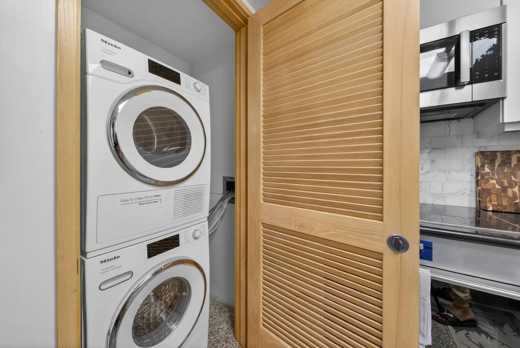 A laundry area with a stacked washer and dryer behind a wooden louvered door.