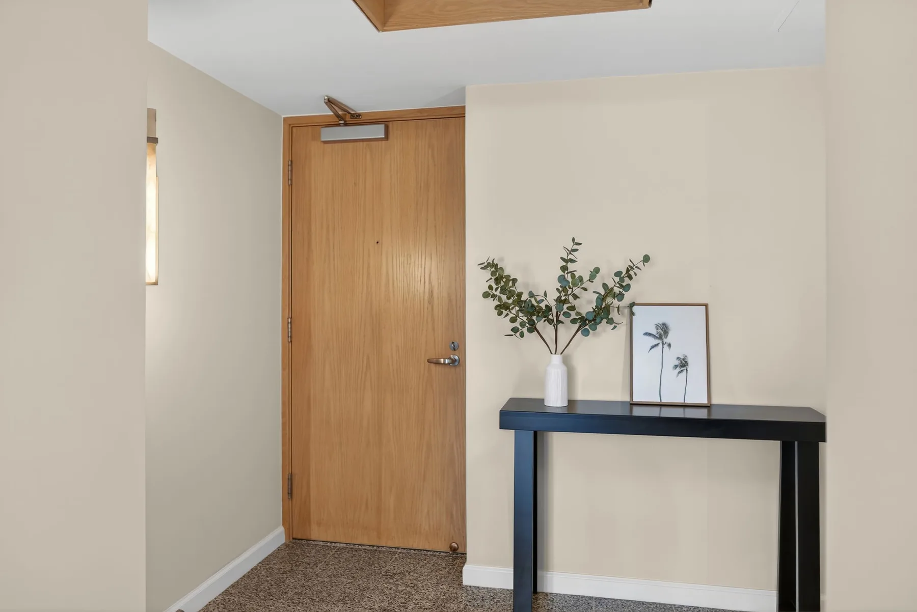 An entryway with a wooden door and a console table topped with a vase.