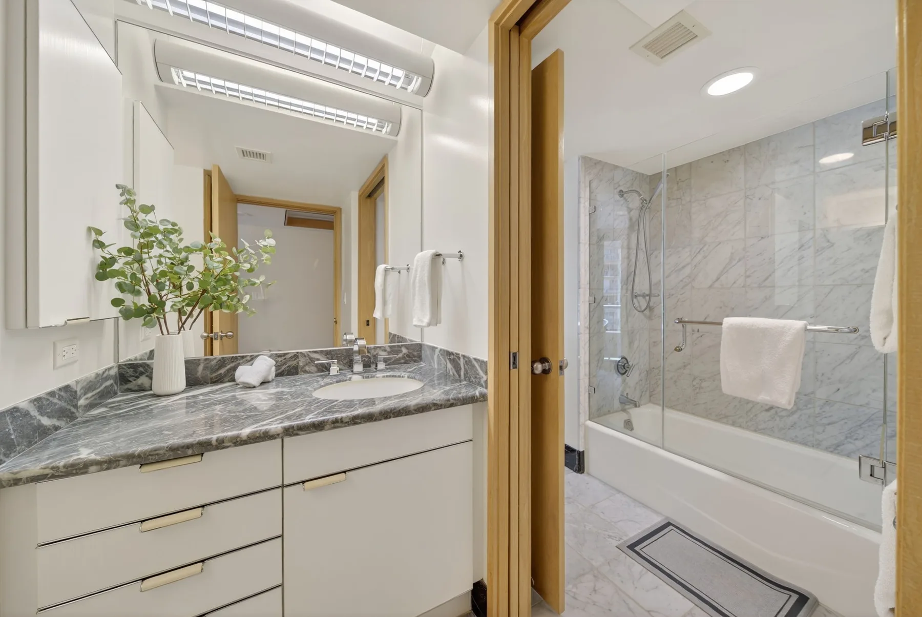 A bathroom vanity with a marble countertop sits beside a glass-enclosed shower.