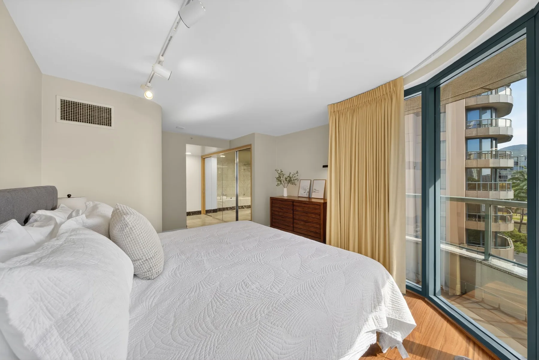 A bright bedroom with a neatly made bed beside large windows.