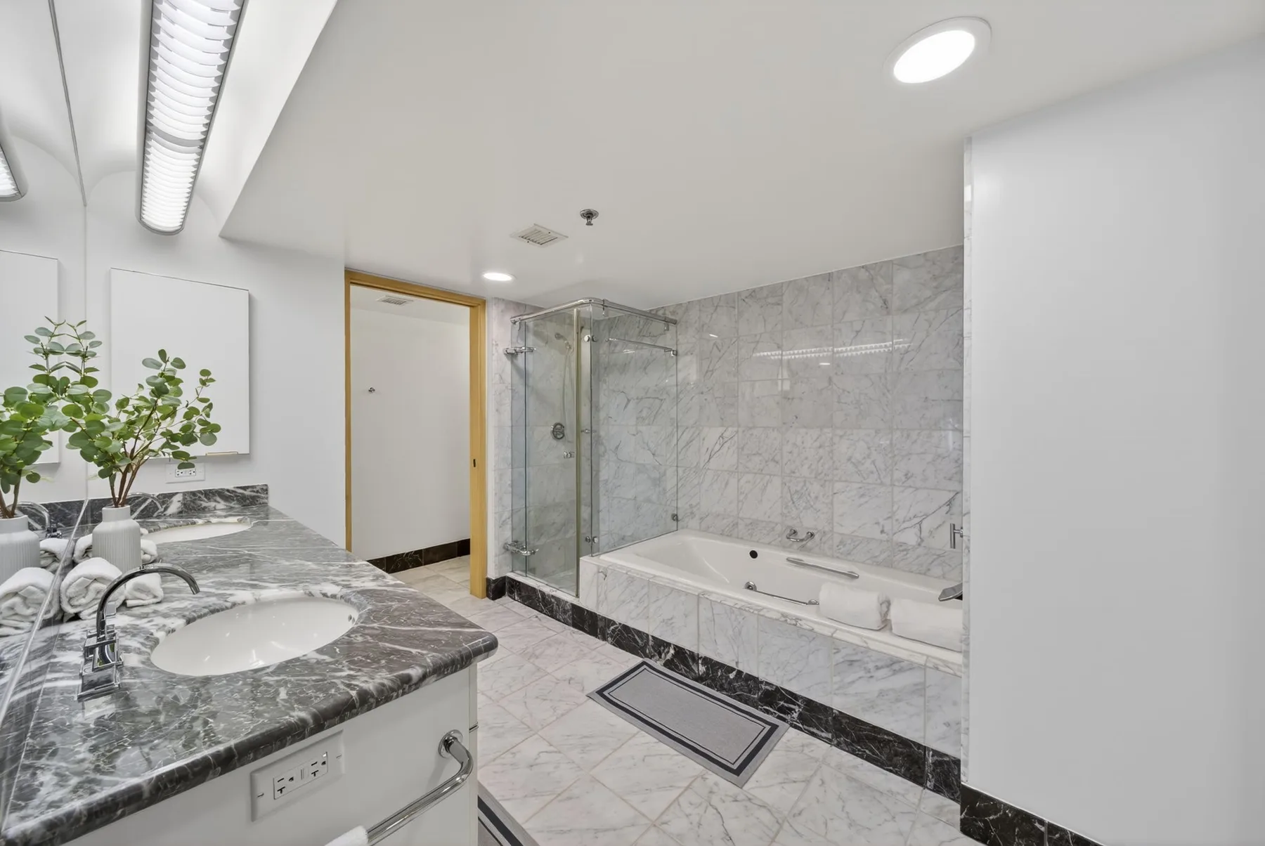A bright bathroom with a marble vanity and a glass-enclosed shower beside a bathtub.