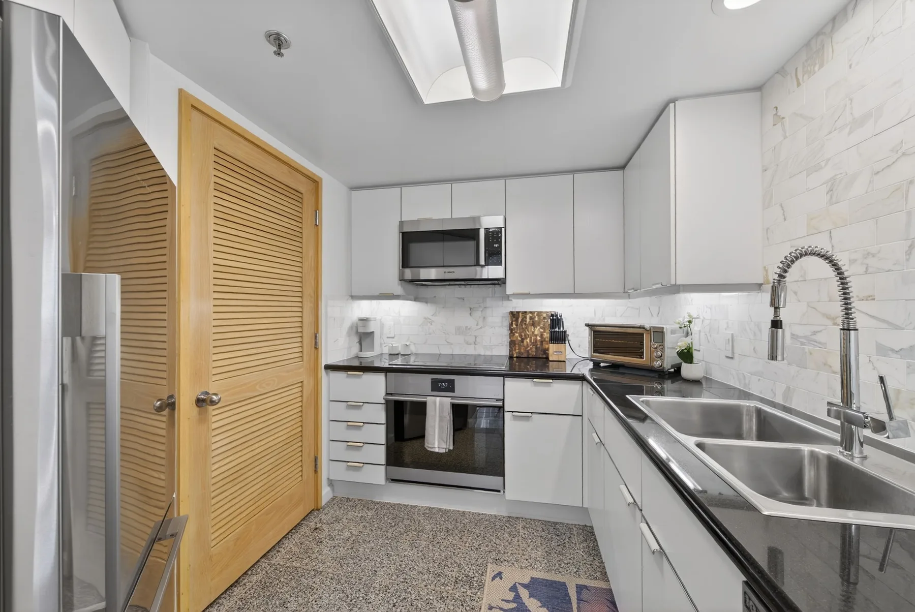 A bright kitchen with white cabinets, stainless steel appliances, and a double sink.