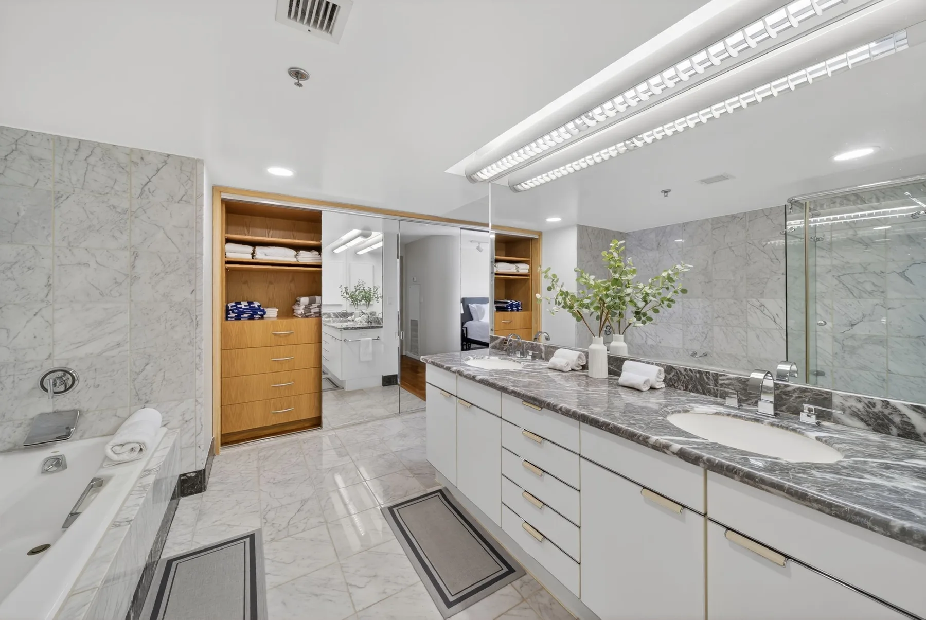A bright marble bathroom features a long vanity and a bathtub.