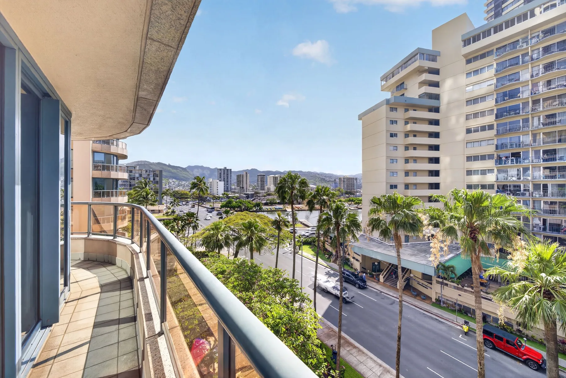 A balcony overlooks a palm-lined street and nearby high-rise buildings.
