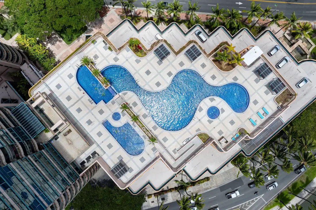 An aerial view shows a large swimming pool surrounded by tiled paving.