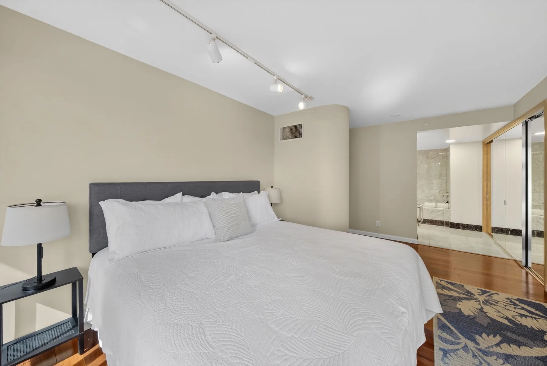 A bedroom with a neatly made bed and a glass-walled bathroom area.