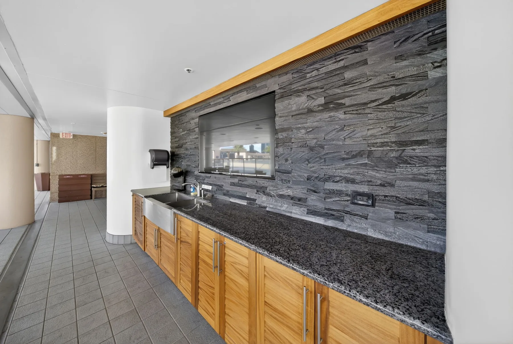A kitchenette with a long counter, wooden cabinets, and a dark tiled backsplash.